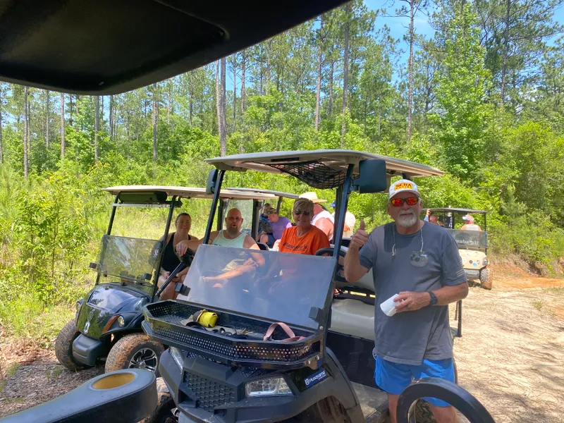 Friends smiling beside a group of golf carts on a sunny wooded road
